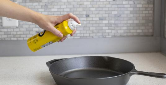 A person sprays the seasoning spray onto a Lodge Cast Iron Skillet.